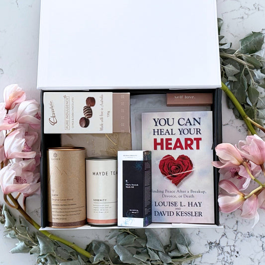 Omoiyari Healing Heart gift hamper box  with self-help book, In memory journal, Body scrub, organic tea, Essentials Oil, Chocolate, and soy candle on a marble surface with flowers.