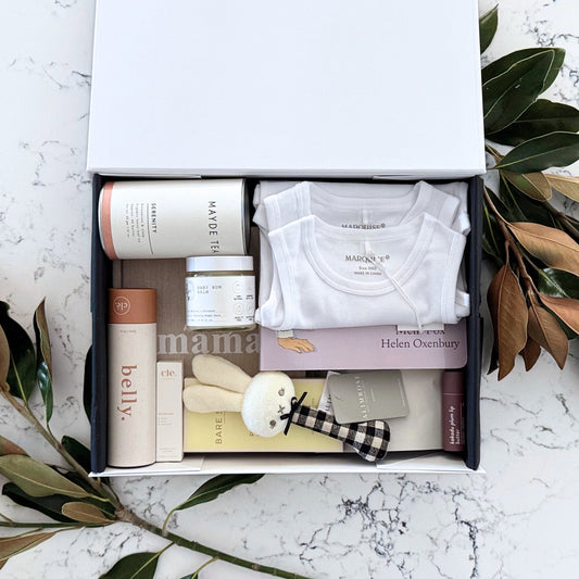 Omoiyari Mum & Baby Luxe gift hamper box - Skincare products, organic tea, stretch mark oil, essential oils, pregnancy journal, pregnancy chocolate and green magnolia leaves on a marble surface