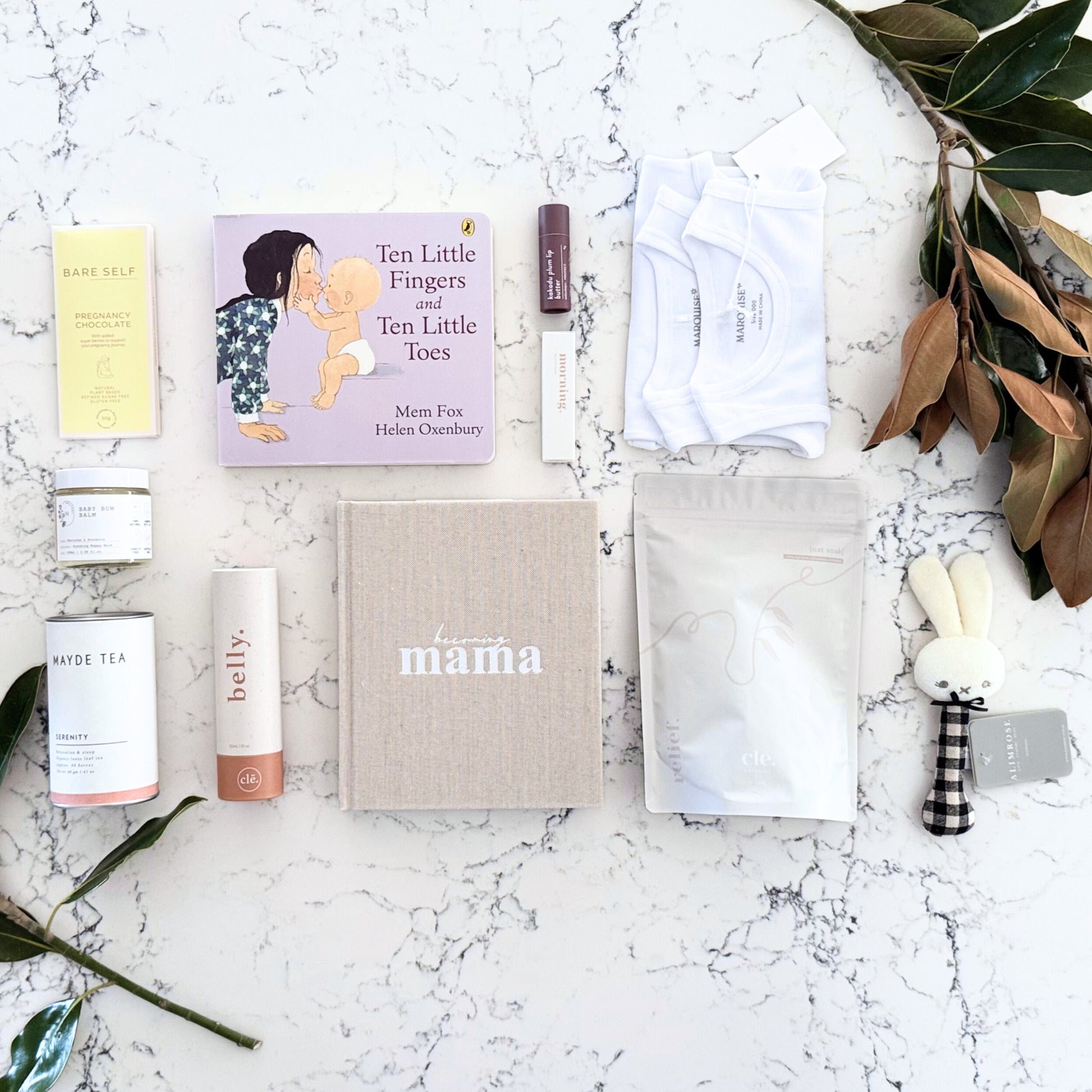 Omoiyari Mum & Baby gift hamper box - Skincare products, organic tea, stretch mark oil, essential oils, pregnancy journal, pregnancy chocolate and green magnolia leaves on a marble surface