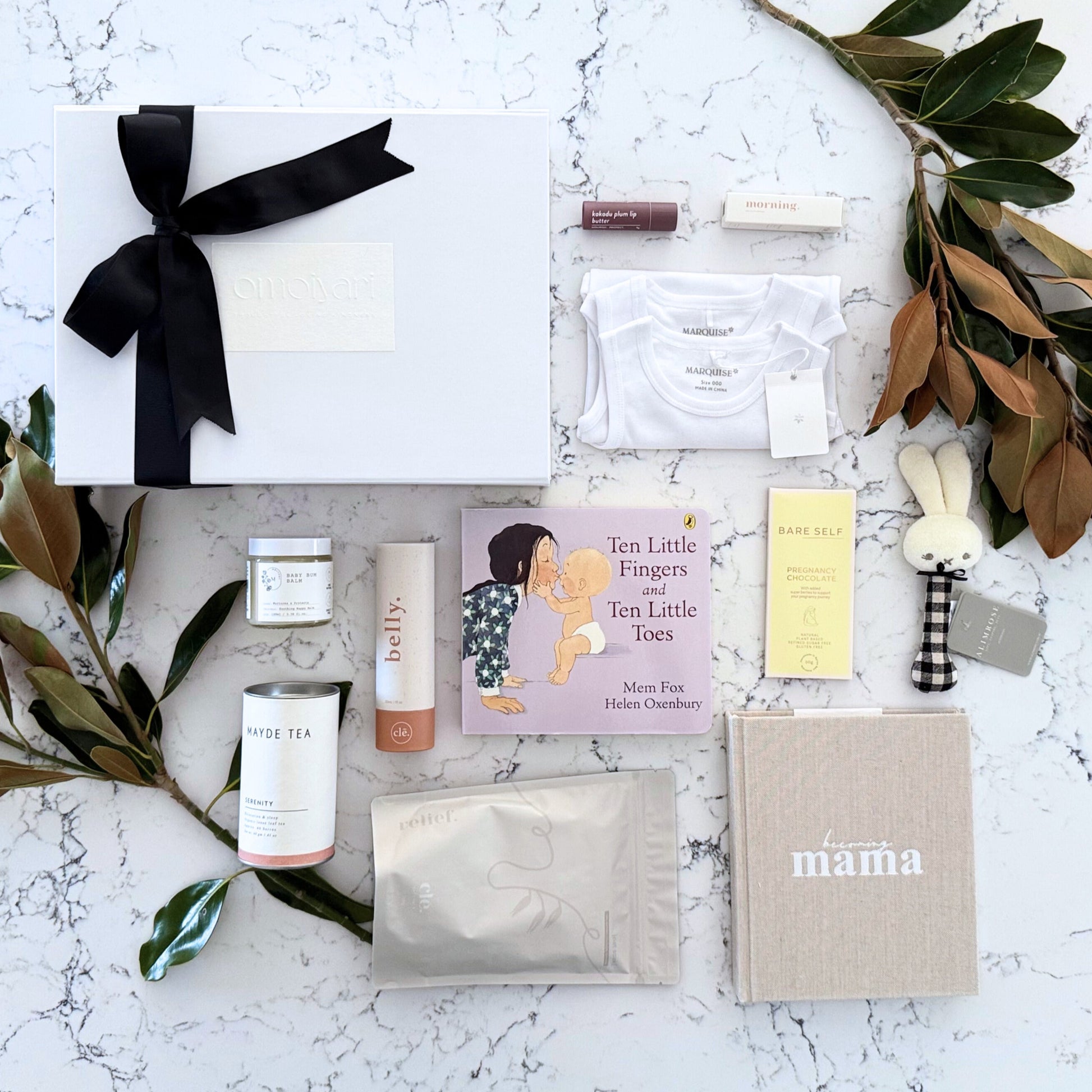 Omoiyari Mum & Baby gift hamper box - Skincare products, organic tea, stretch mark oil, essential oils, pregnancy journal, pregnancy chocolate and green magnolia leaves on a marble surface