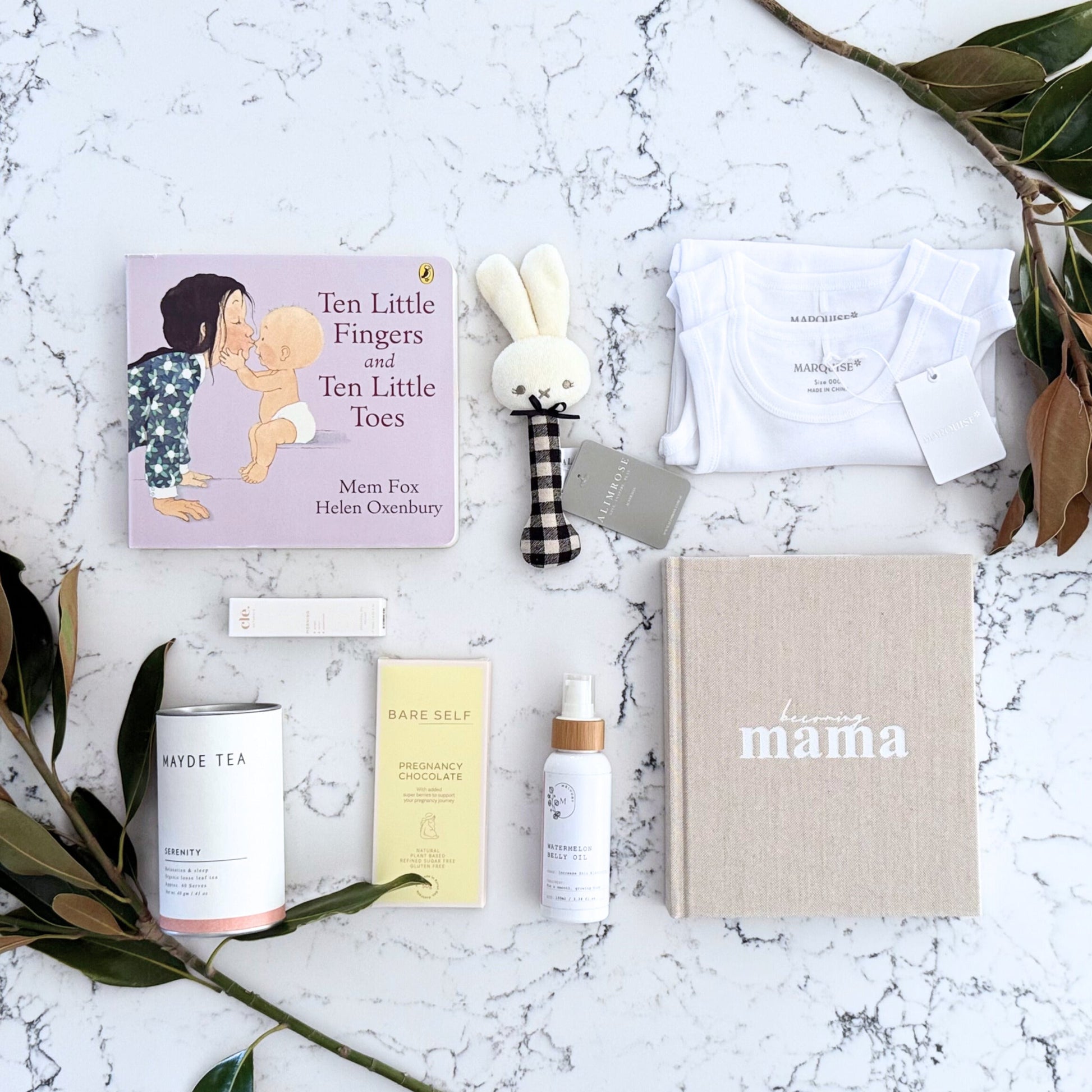 Omoiyari Mum & Baby gift hamper box - Skincare products, organic tea, stretch mark oil, essential oils, pregnancy journal, pregnancy chocolate and green magnolia leaves on a marble surface