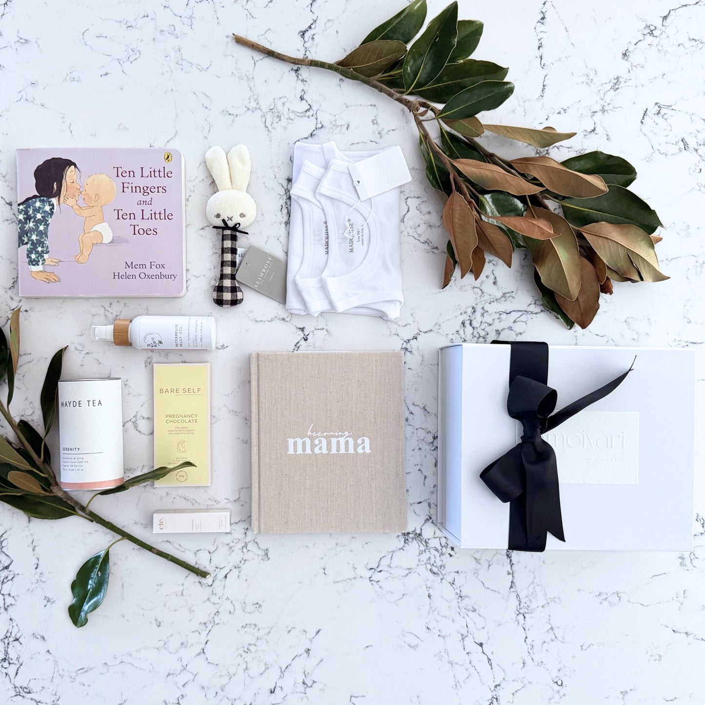 Omoiyari Mum & Baby gift hamper box - Skincare products, organic tea, stretch mark oil, essential oils, pregnancy journal, pregnancy chocolate and green magnolia leaves on a marble surface