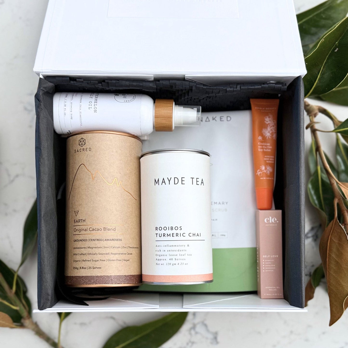 Omoiyari Glow & Grow gift hamper box - Skincare products, organic cacao and tea, stretch mark oil, lip balm and green magnolia leaves on a marble surface
