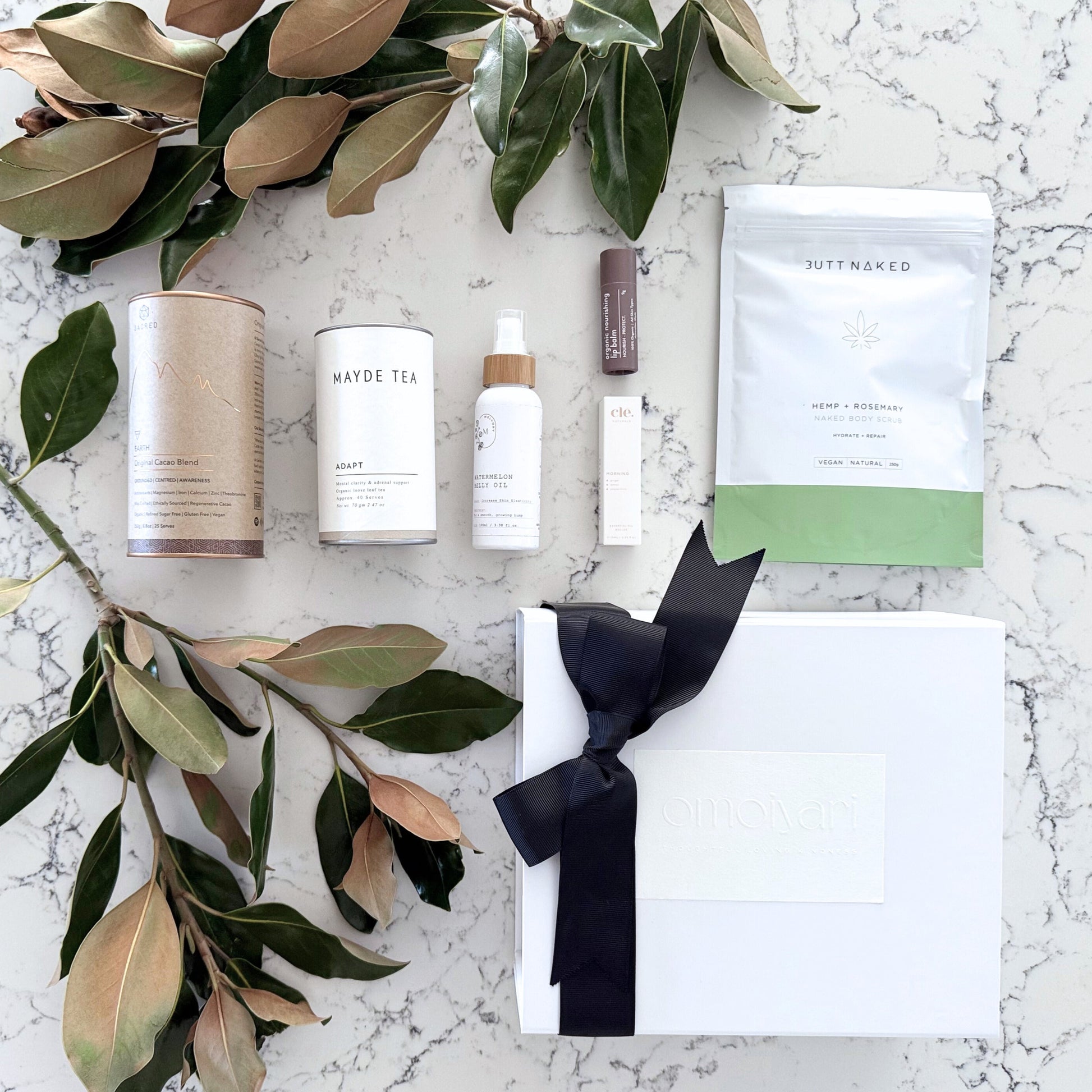 Omoiyari Nurture & Nourish gift hamper box - Skincare products, organic cacao and tea, stretch mark oil, lip balm and green magnolia leaves on a marble surface