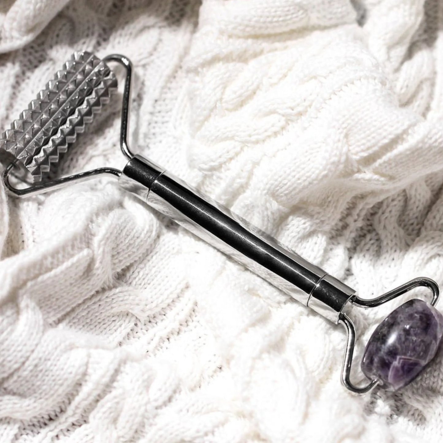 Massage tool with textured end and purple stone on a white textured surface