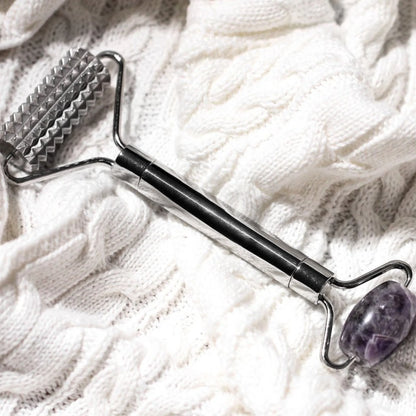 Massage tool with textured end and purple stone on a white textured surface